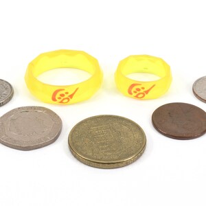 May include: Two yellow silicone rings with a red logo, surrounded by six coins of different sizes and colors.
