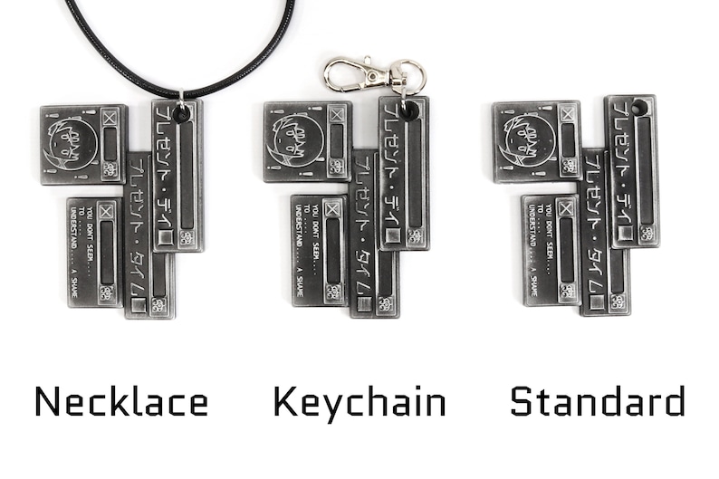 May include: A silver-toned metal pendant necklace, keychain, and standard charm featuring a stylized image of a character's face with the text "プレゼント・タイム" (present time) in Japanese. The charm is made up of five interlocking pieces.