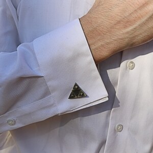 May include: A white dress shirt with a pair of cufflinks featuring a silver triangular design with black and white details.