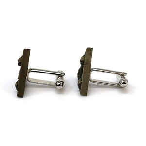 May include: A pair of cufflinks with a square, textured, dark brown design. The cufflinks are made of metal and have a silver-toned finish.