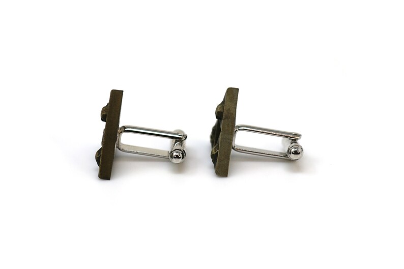 May include: A pair of cufflinks with a square, textured, dark brown design. The cufflinks are made of metal and have a silver-toned finish.