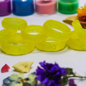 May include: A group of six bright yellow silicone rings with a raised design. The rings are stacked on top of each other and are on a white surface.