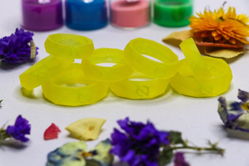 May include: A group of six bright yellow silicone rings with a raised design. The rings are stacked on top of each other and are on a white surface.