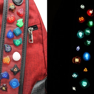 May include: A red backpack with a black strap and a row of glowing, colourful, circular pins with various symbols. The pins glow in the dark.