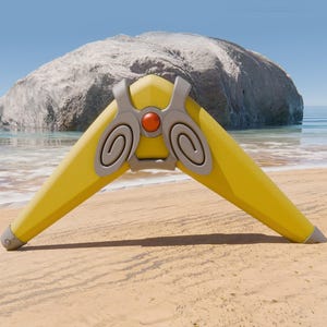 Puede incluir: Un boomerang amarillo con detalles grises y un bot&oacute;n circular rojo en el centro. El boomerang est&aacute; en una playa de arena con una gran roca en el fondo.