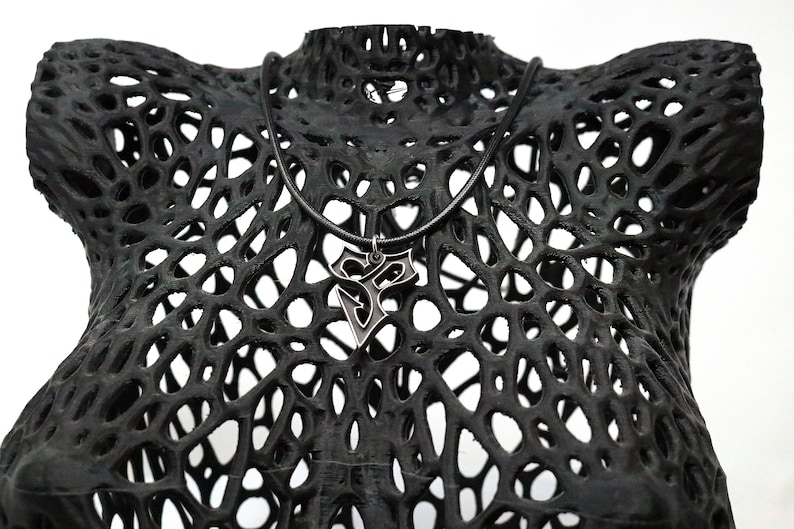May include: A black, 3D printed, geometric, lattice-like sculpture with a silver pendant necklace hanging from it.