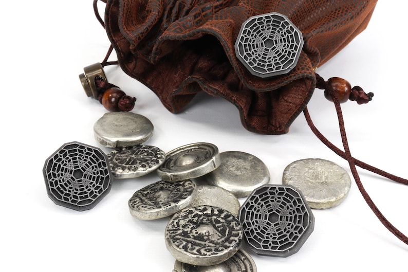 May include: A brown leather pouch with a drawstring closure, spilling out silver and gray metal tokens. The tokens feature a geometric design.