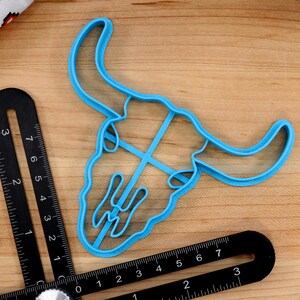 May include: A blue plastic cookie cutter shaped like a bull skull. The cutter is approximately 3 inches wide and 4 inches tall.