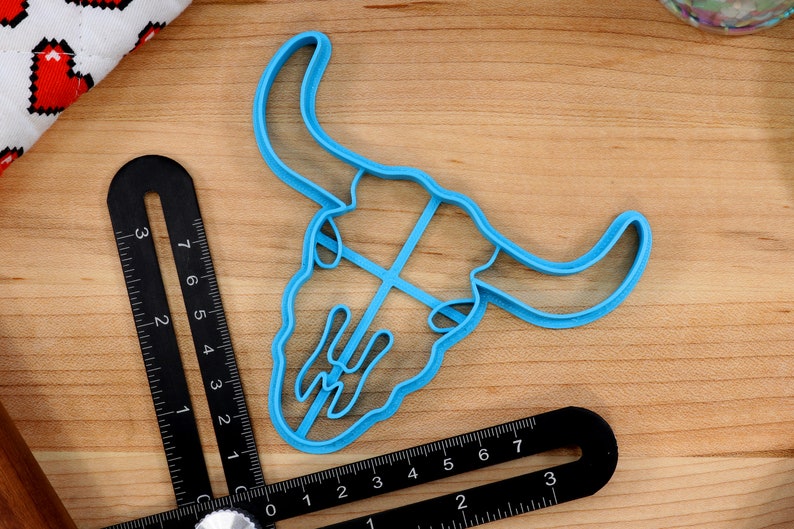 May include: A blue plastic cookie cutter shaped like a bull skull. The cutter is approximately 3 inches wide and 4 inches tall.