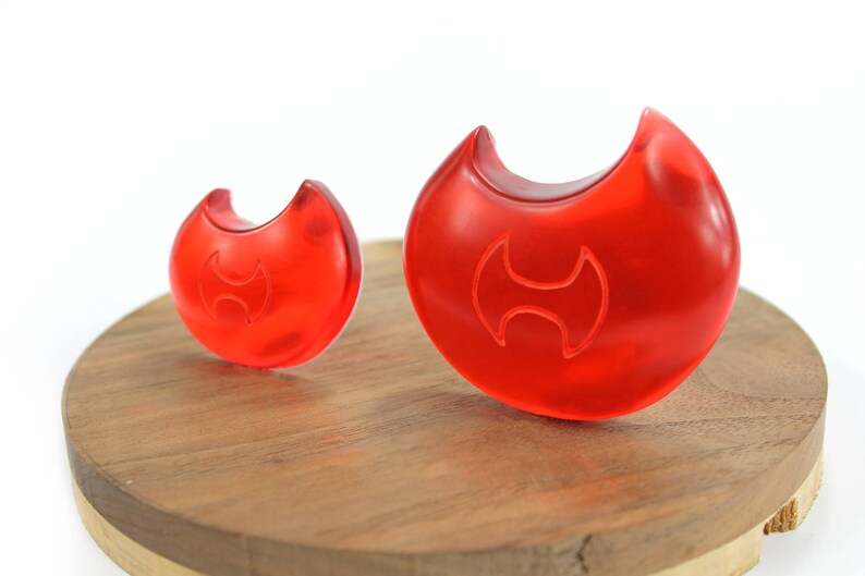 May include: Two red plastic objects shaped like a crescent moon with a stylized H design in the center. The objects are on a wooden surface.
