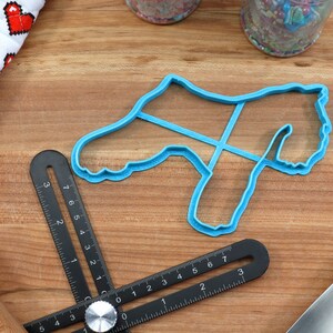 May include: A blue plastic cookie cutter shaped like a dog on a wooden surface with a black ruler and a rolling pin.