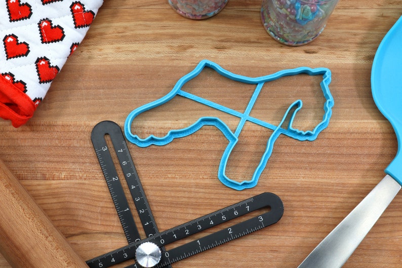 May include: A blue plastic cookie cutter shaped like a dog on a wooden surface with a black ruler and a rolling pin.