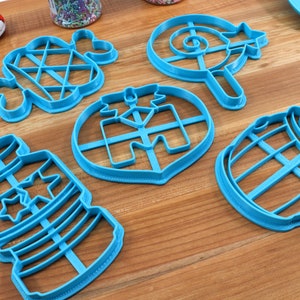 Puede incluir: Un juego de seis cortadores de galletas de pl&aacute;stico azul con forma de botella, barril, piruleta, estrella, coraz&oacute;n y diamante. Los cortadores est&aacute;n sobre una superficie de madera.