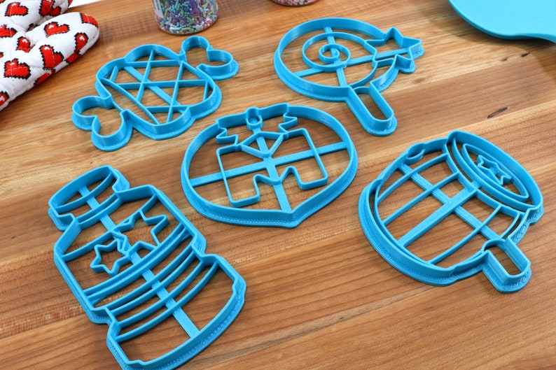 Puede incluir: Un juego de seis cortadores de galletas de pl&aacute;stico azul con forma de botella, barril, piruleta, estrella, coraz&oacute;n y diamante. Los cortadores est&aacute;n sobre una superficie de madera.