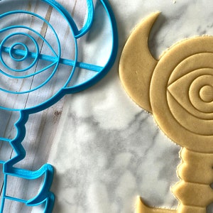 Op de afbeelding: Een blauwe plastic koekjesvormer in de vorm van een sleutel met een oogontwerp. Een koekje wordt uitgestoken met de vormer.