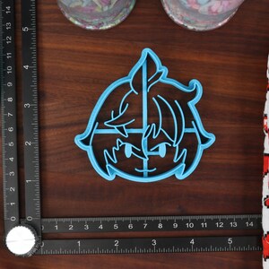 May include: A blue plastic cookie cutter shaped like a cartoon character with a sword. The character has short, spiky hair and is wearing a blue shirt.