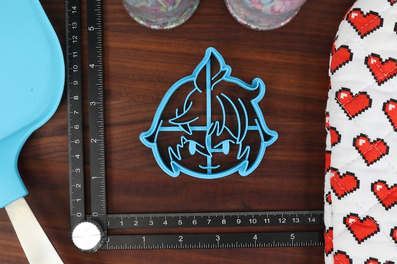 May include: A blue plastic cookie cutter shaped like a cartoon character with a sword. The character has short, spiky hair and is wearing a blue shirt.