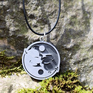 May include: A silver necklace with a yin yang pendant featuring a black and white design of two stylized faces.