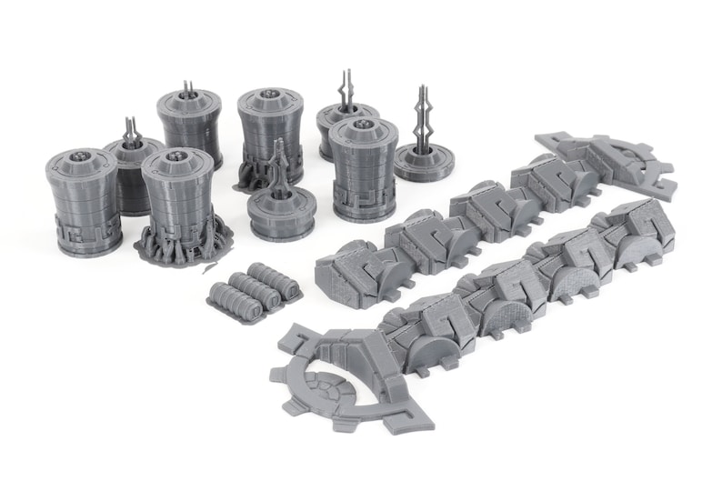 May include: A set of gray 3D printed model pieces for a sci-fi spaceship. The set includes a variety of shapes, including cylinders, squares, and rectangles. The pieces are designed to be assembled together to create a complete spaceship model.
