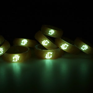 May include: A stack of eight glow-in-the-dark silicone rings with a white "J" logo. The rings are stacked in a pyramid shape and are illuminated in a dark room.