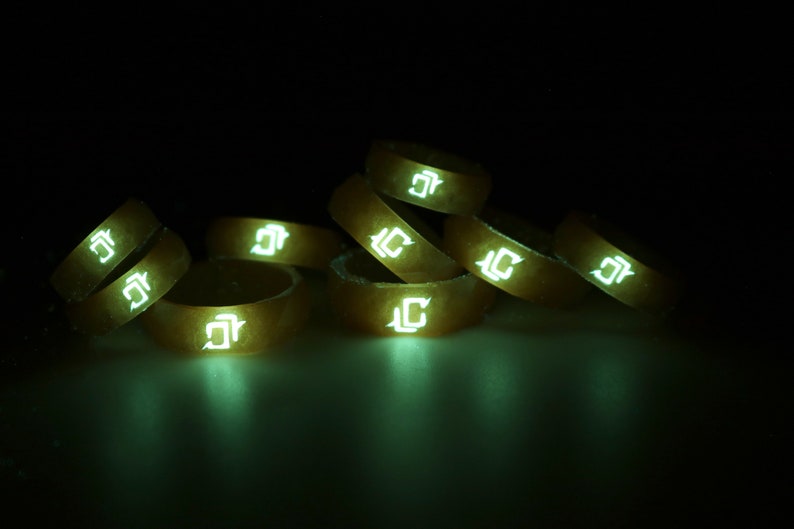 May include: A stack of eight glow-in-the-dark silicone rings with a white "J" logo. The rings are stacked in a pyramid shape and are illuminated in a dark room.