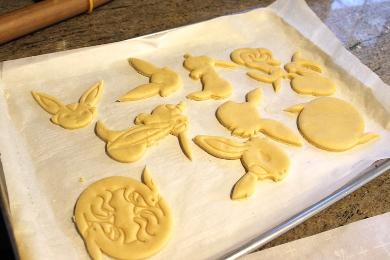 May include: A baking sheet with unbaked sugar cookies cut into various shapes, including a unicorn, a bunny, and a character from a popular video game.