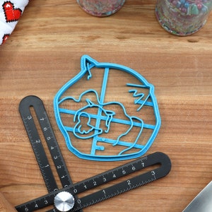 May include: A blue plastic cookie cutter shaped like a cartoon animal with a large head and a small body. The cutter has a detailed design with lines and curves.