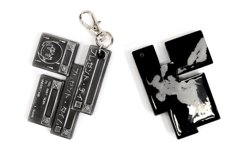 May include: Two metal keychains, one silver and one black, with a geometric design. The silver keychain has the text "プレゼント・タイム" and "YOU DON'T SEEM... TO... UNDERSTAND... A SHAME" on it.