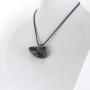 Puede incluir: Un collar con un colgante de ocarina de color plateado y un cord&oacute;n negro. La ocarina tiene un dise&ntilde;o detallado con varios agujeros.