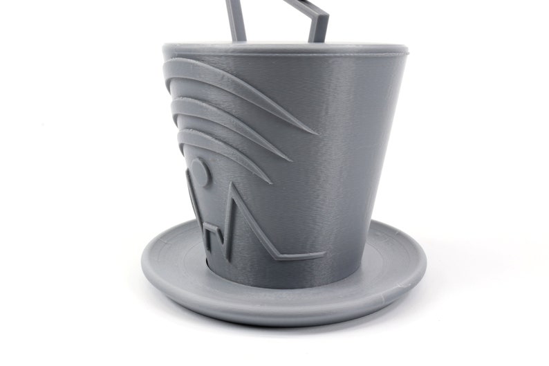 Pode incluir: Um chap&eacute;u cinza impresso em 3D com um design geom&eacute;trico e um pires correspondente. O chap&eacute;u tem um design em relevo na frente.