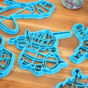 May include: Set of six blue plastic cookie cutters shaped like knights and a ship. The cutters are on a wooden surface.