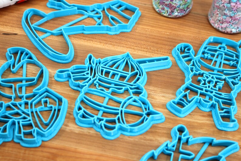 May include: Set of six blue plastic cookie cutters shaped like knights and a ship. The cutters are on a wooden surface.