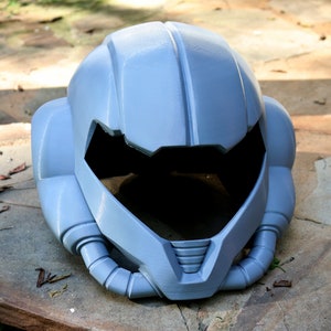 May include: A gray, futuristic-looking helmet with a large visor and intricate details. The helmet is made of a smooth, hard plastic and has a slightly textured surface.