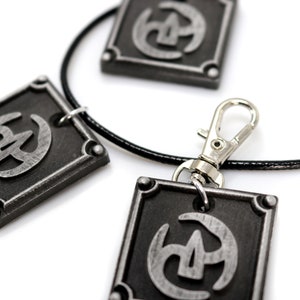 May include: A black leather necklace with three silver square pendants. Each pendant features a stylised silver symbol.