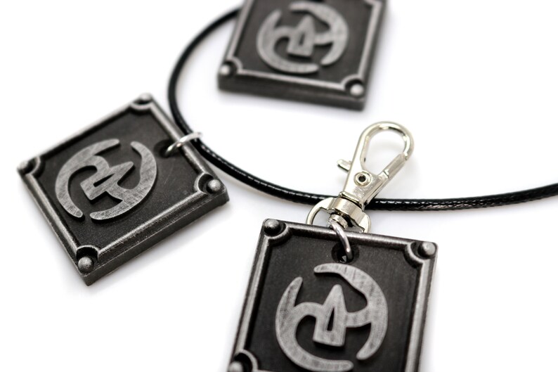 May include: A black leather necklace with three silver square pendants. Each pendant features a stylised silver symbol.