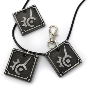 May include: Three silver-colored pendants with a black and white symbol on each. The pendants are attached to a black cord necklace with a silver clasp.