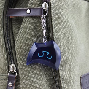 May include: A blue and silver keychain with a blue symbol on it. The keychain is attached to a green canvas bag.