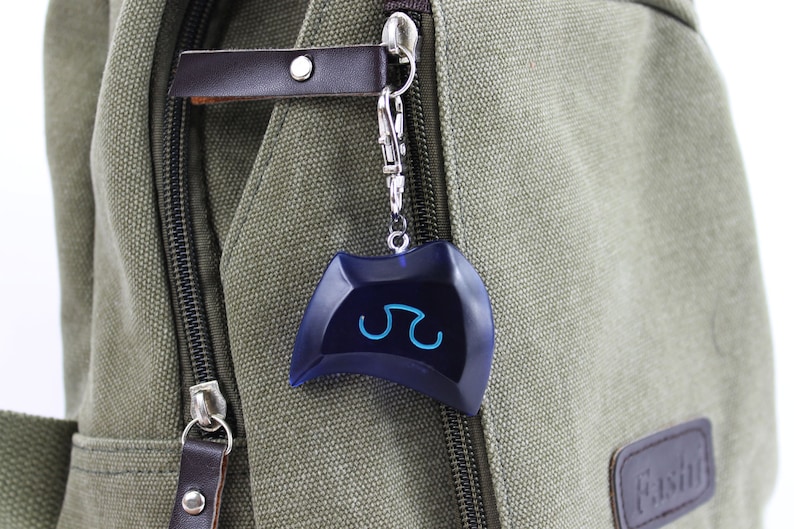May include: A blue and silver keychain with a blue symbol on it. The keychain is attached to a green canvas bag.