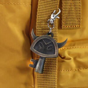 May include: A gold-colored key charm with a shield and horns, attached to a yellow backpack strap.