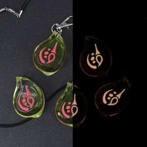 May include: A black necklace with a silver clasp and four green glass pendants. Each pendant has a pink symbol inside. The pendants glow in the dark, with the symbols appearing white.