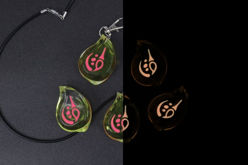 May include: A black necklace with a silver clasp and four green glass pendants. Each pendant has a pink symbol inside. The pendants glow in the dark, with the symbols appearing white.