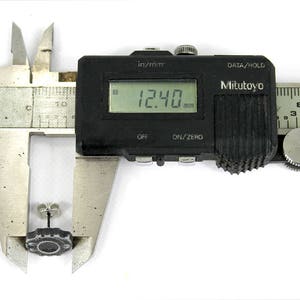 May include: A black digital caliper measuring a small, dark gray object. The caliper reads 12.40 mm.