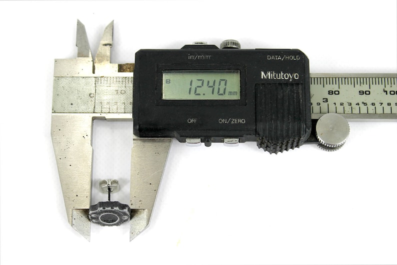 May include: A black digital caliper measuring a small, dark gray object. The caliper reads 12.40 mm.