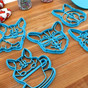 Pu&ograve; includere: Cinque tagliabiscotti in plastica blu a forma di corgi. I tagliabiscotti presentano diversi design di corgi, tra cui un corgi con gli occhiali, un corgi che tiene una tazza di caff&egrave; e un corgi con la lingua di fuori.