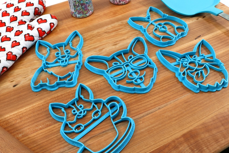 Pu&ograve; includere: Cinque tagliabiscotti in plastica blu a forma di corgi. I tagliabiscotti presentano diversi design di corgi, tra cui un corgi con gli occhiali, un corgi che tiene una tazza di caff&egrave; e un corgi con la lingua di fuori.