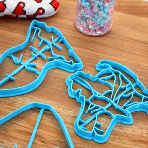 May include: Four blue plastic cookie cutters shaped like different flowers on a wooden surface.
