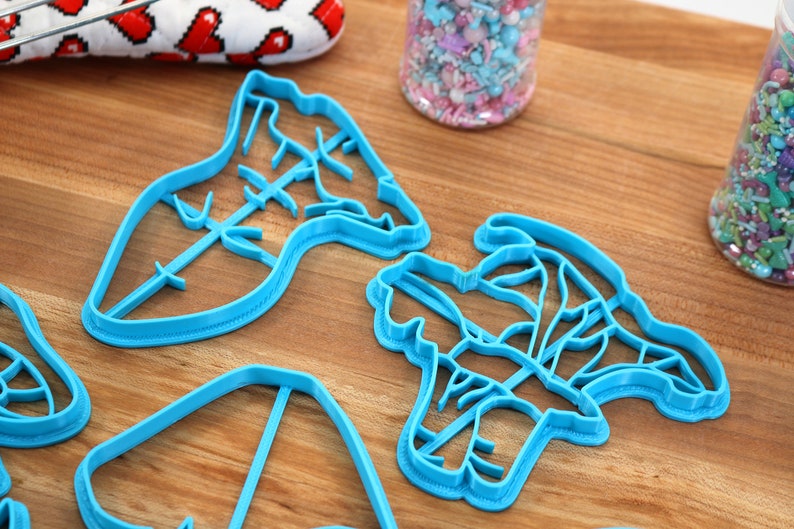 May include: Four blue plastic cookie cutters shaped like different flowers on a wooden surface.