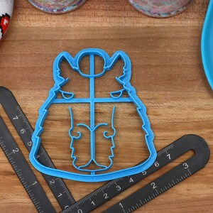 May include: Blue plastic cookie cutter shaped like a cartoon husky dog. The cutter is on a wooden surface with a ruler and a blue plate.
