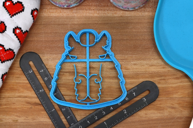 May include: Blue plastic cookie cutter shaped like a cartoon husky dog. The cutter is on a wooden surface with a ruler and a blue plate.
