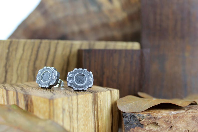 May include: A pair of silver-colored metal earrings with a circular design. The earrings are on a wooden surface.